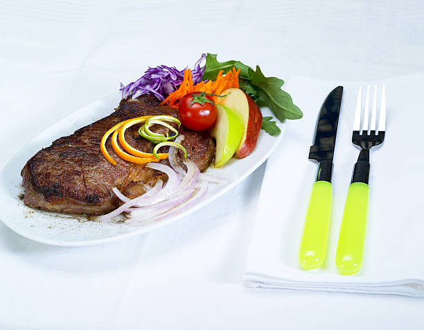 Ribeye steak, fruit, and vegetables with yellow utensils. 