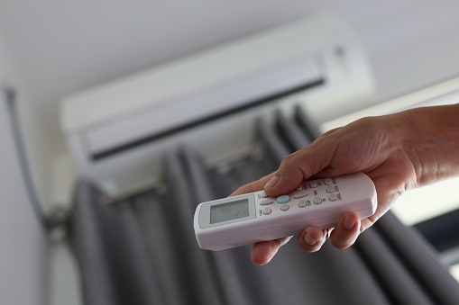 A woman's hand holds the remote control and turns on the home air conditioner