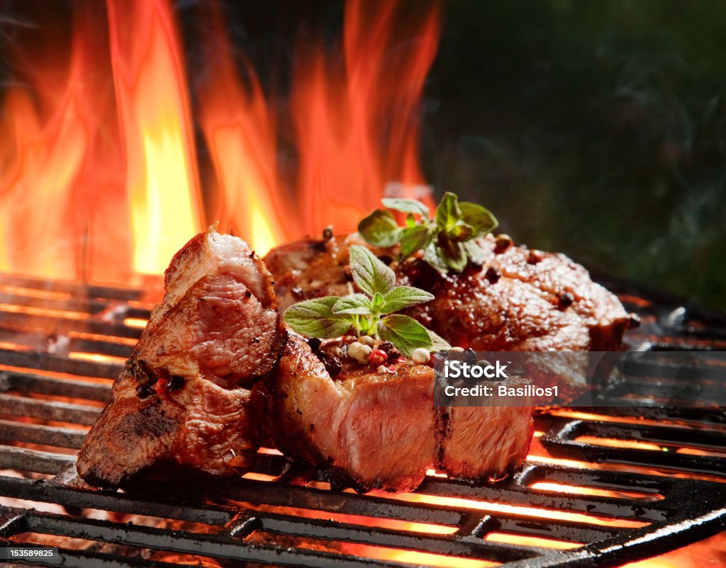 Beef steaks in the flames Grilled thick beef steaks with seven types of pepper (peppercorn) and mint leafs on a grill, flames Barbecue - Meal Stock Photo