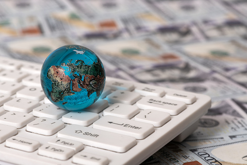 Glass globe on a computer keyboard against the background of 100 US dollar bills