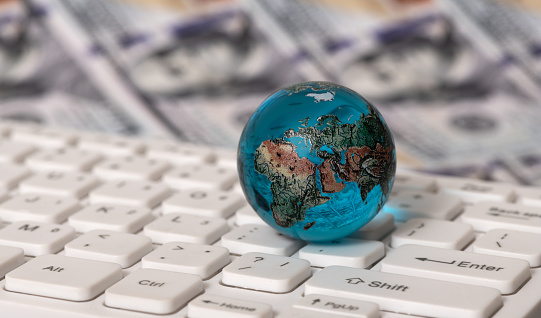 Glass globe on a computer keyboard against the background of 100 US dollar bills