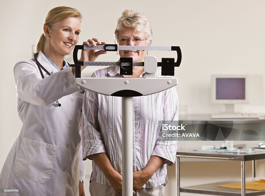 Doctor weighing senior woman Doctor weighing senior woman in doctor office Weight Scale Stock Photo