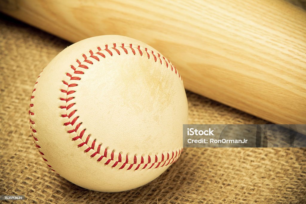 Baseball This is a shot of an old baseball next to a wooden bat on a burlap sack background. Shot in a warm, retro color ton with vignetting. Baseball - Ball Stock Photo