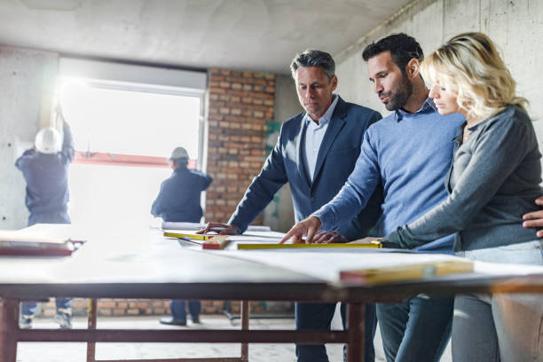 istock Young couple and their agent examining blueprints at construction site. 1536003012