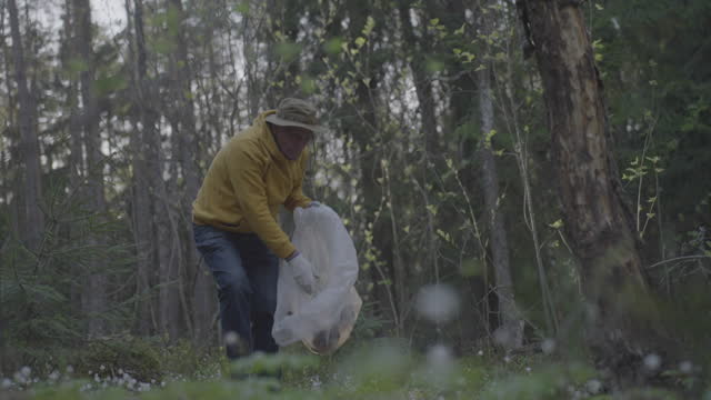 Mature man collects litter in wood caring about nature
