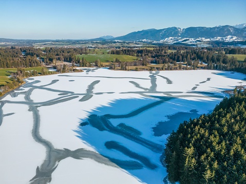 An aerial shot of an idyllic Allgaeu winter landscape with snow-covered trees, and rolling hills
