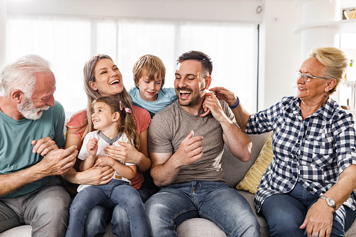 Smiling multi-generation family petting their golden retriever while sitting together on a sofa in their living room at home