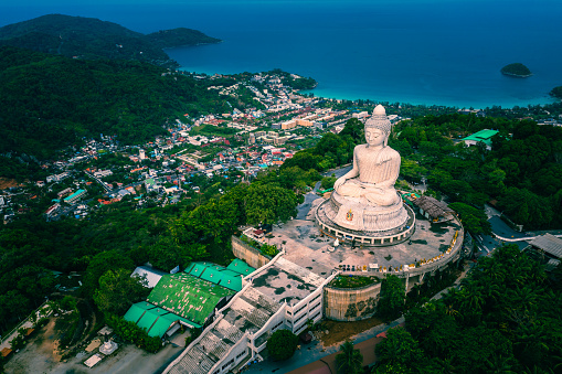 Big buddha statue in Phuket Thailand against blue sky with clouds and ocean.