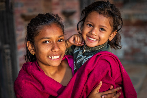 Nepali girls holding her little sister on the Durbar Square of Bhaktapur. Bhaktapur is an ancient town in the Kathmandu Valley and is listed as a World Heritage Site by UNESCO for its rich culture, temples, and wood, metal and stone artwork.