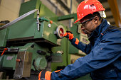 A dark-skinned industrial worker prepares a metalworking machine for work