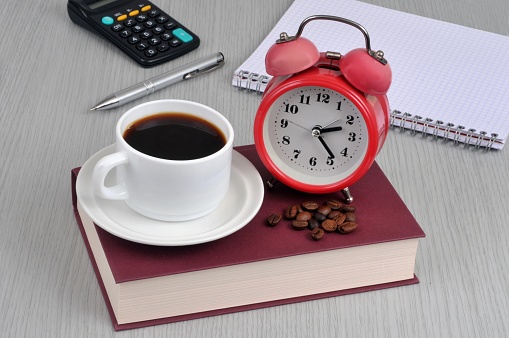 Cup of coffee and alarm clock on a book