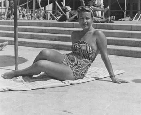 After swimming. Smiling senior woman standing at the swimming pool with a towel on shoulder