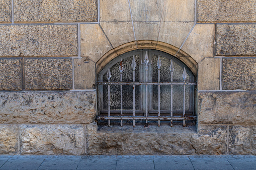 Arched basement window in a stone wall with beautiful wrought iron bars.