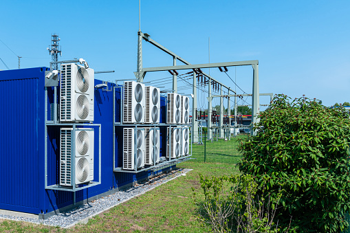 Transformer power station with large cooling fans on the rear wall. Blue sky and green bushes.