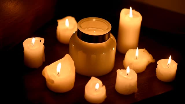 Lots of candles burning in the dark. Romantic evening. Candles are corrected and hands. Taking care of home, comfort and warmth