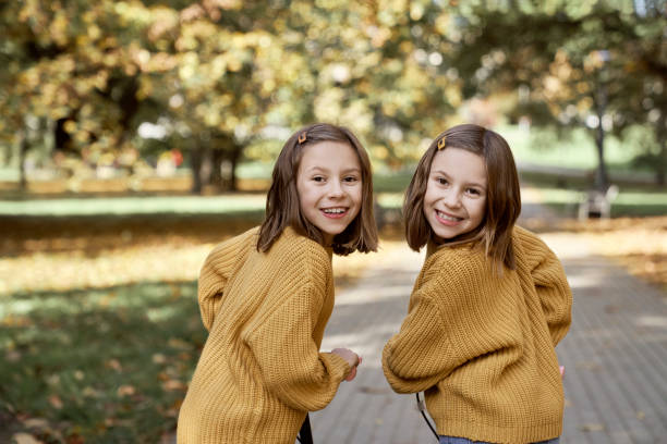 Friends ages 10 and 11 sitting outdoors on a bench by a tree. They are wearing similar clothes.
