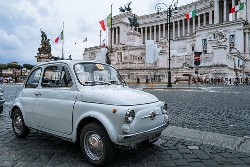 Rome, Italy, June 4, 2023: Vintage car parade on June 4, 2023 in Roma, Italy. Old vintage cars are parked in front of Vittorio Emanuele Monument, participating to a parade. A Fiat 500 attract people attention