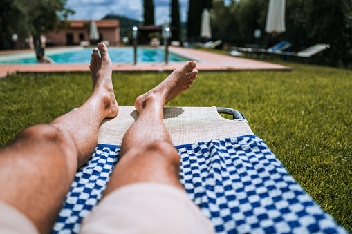 POV of summer relaxing and sunbathing by swimming pool: man feet while resting under a warm sun in Italy