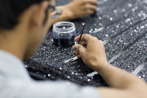Closeup of handicraft tailor embroidering black sequins beads onto tulle at the workshop. Making a couture dress.