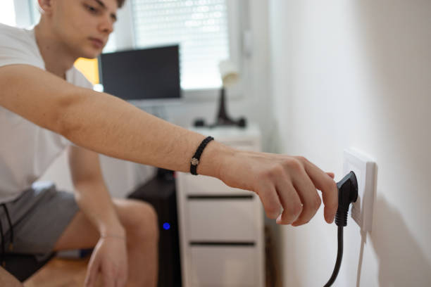 ragazzo adolescente, collegare il cavo del computer alla presa elettrica - electric plug outlet human hand electricity foto e immagini stock