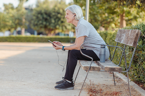 Older woman sitting on a park bench with a mobile phone. horizontal