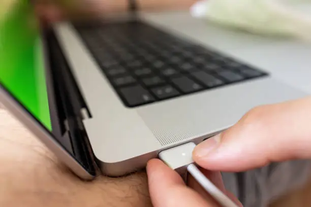 Photo of Close-up of teenage boy, inserting Max safe charger into USB port on the MacBook Pro