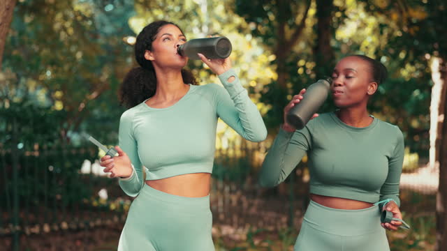 Fitness, drinking water and friends with women in park for running, training and bonding. Relax, happy and break with female runner and toast with bottle in nature for workout, exercise and wellness