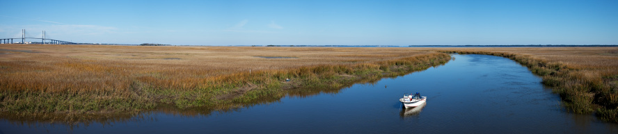 Georgia coast Jekyll island wetlands panorama with stream and small fishing boat. Sydney Lanier bridge in the background to the left.