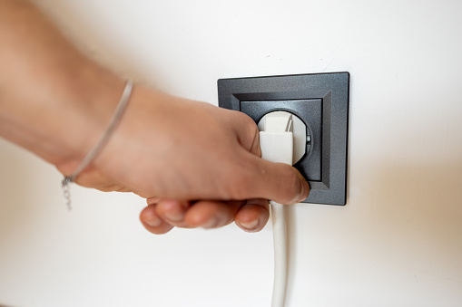 Close up of unrecognizable Caucasian teenage boy, plug-in extension cord into electrical outlet