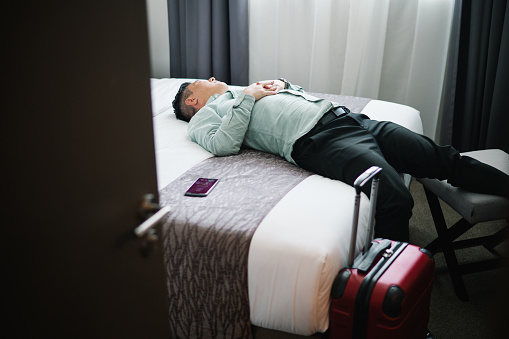 Businessman lying on hotel bed exhausted from the business trip with business wear.