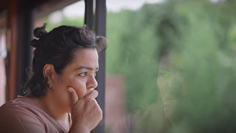 Mujer latina angustiada sintiéndose preocupada y estresada mientras mira por una ventana. Malas noticias.