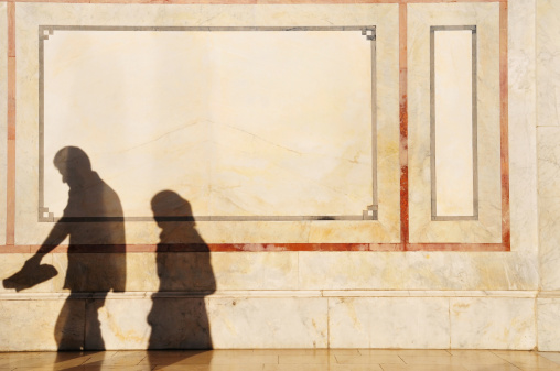 The shadow of a Syrian couple walking through the courtyard of the Umayyad Mosque in Damascus, Syria. The man is holding his shoes. the woman is wearing a head scarf.