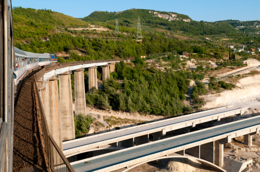 A train passes over a railway bridge, which itself is built over a highway bridge (still under construction). Location: between Aleppo and Latakia, Syria.