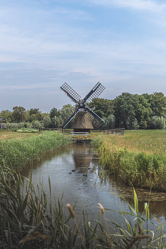 wooden windmill stands by the water in a field in the Netherlands