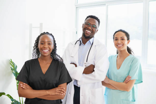 Three medical healthcare professionals stand in a row smiling arms folded stock photo