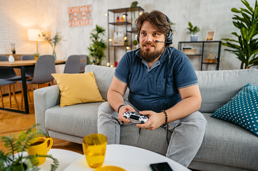 Overweight young man playing video games on a joystick at home.
