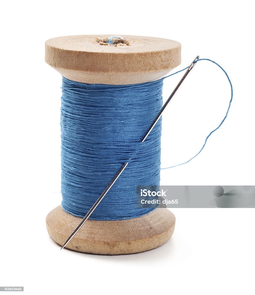 A spool of blue thread with a needle in it Spool of thread with needle isolated on white Thread - Sewing Item Stock Photo