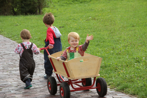 Girl and boy pulling their brother sitting in a handcart