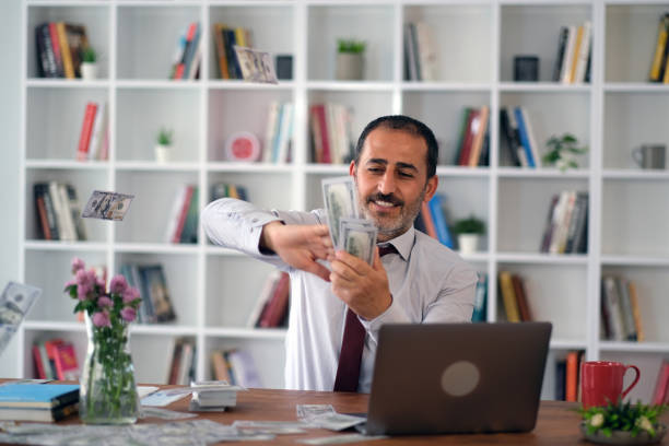 istock Businessman happily scatters dollar bills at workplace in modern office 1536568182