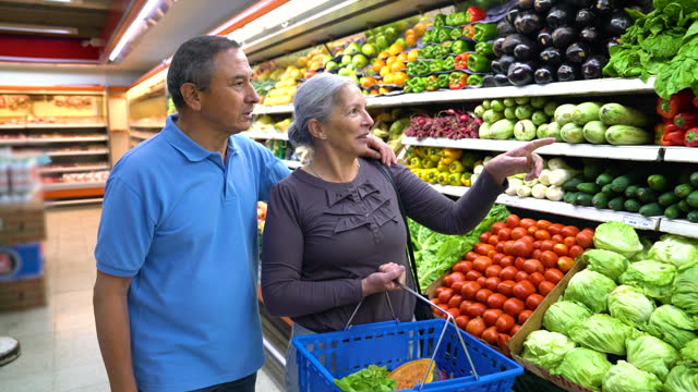Senior couple at the supermarket shopping together talking and smiling while walking by the refrigerated produce section