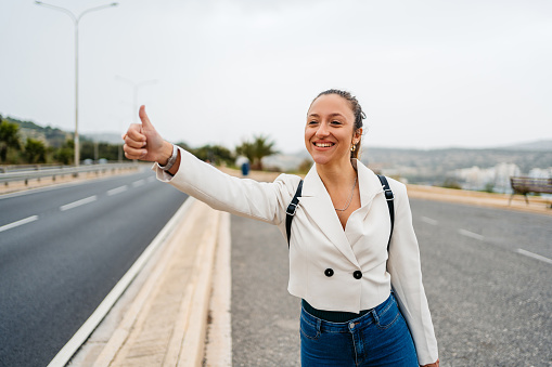 Beautiful young woman standing next to a highway road and hitchhiking in Malta.