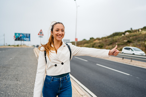 Beautiful young woman standing next to a highway road and hitchhiking in Malta.