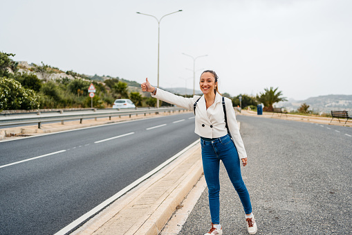 Beautiful young woman standing next to a highway road and hitchhiking in Malta.