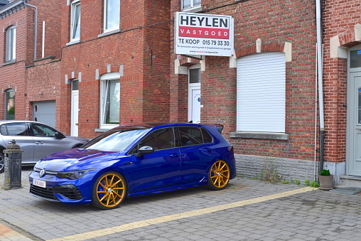 Wilsele, Vlaams-Brabant, Belgium - July 12, 2023: parked heavy blue color German car with golden wheel spokes in front of a house to sale by Heylen properties