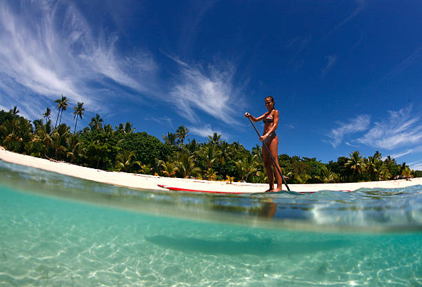 stand up paddle boarding in Fiji a young woman enjoys stand-up paddle boarding in the tropical waters of Fiji fiji stock pictures, royalty-free photos & images