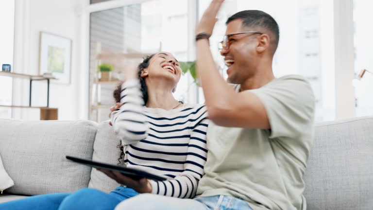 Couple, tablet and high five on sofa in home living room with celebration, winning and happiness for online gaming. Man, woman and mobile touchscreen for crypto, esport competition or winner in house