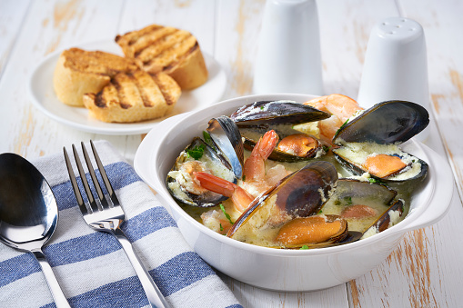 Creamy soup with seafood mussels and prawns on a white table.