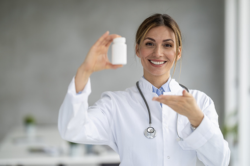 Portrait of female doctor holding bottle of medicaments and showing free space.Copy space.