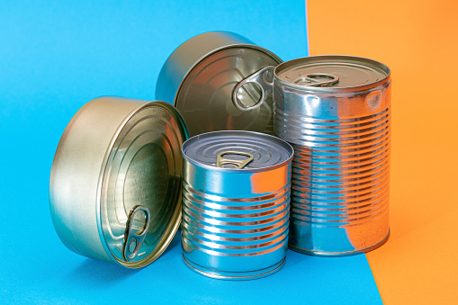 A Group of Stacked Tin Cans with Blank Edges on Split Blue and Orange Background. Canned Food. Different Aluminum Cans for Safe and Long Term Storage of Food. Steel Sealed Food Storage Containers