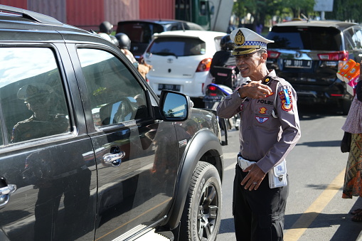 Smiling thai traffic police officer in conversation at promenade of Mekong river in Nakhon Phanom in morning. In background are more people and another office. Policemen are wearing barrets